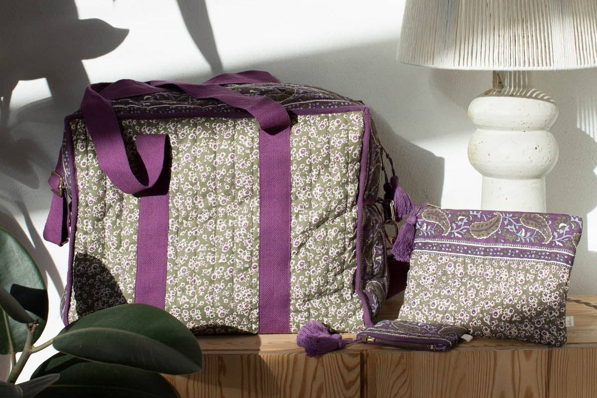 Decorative box with a purple ribbon on a wooden surface with a lamp and plant in the background.