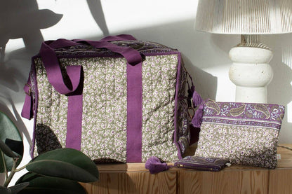 Decorative box with a purple ribbon on a wooden surface with a lamp and plant in the background.